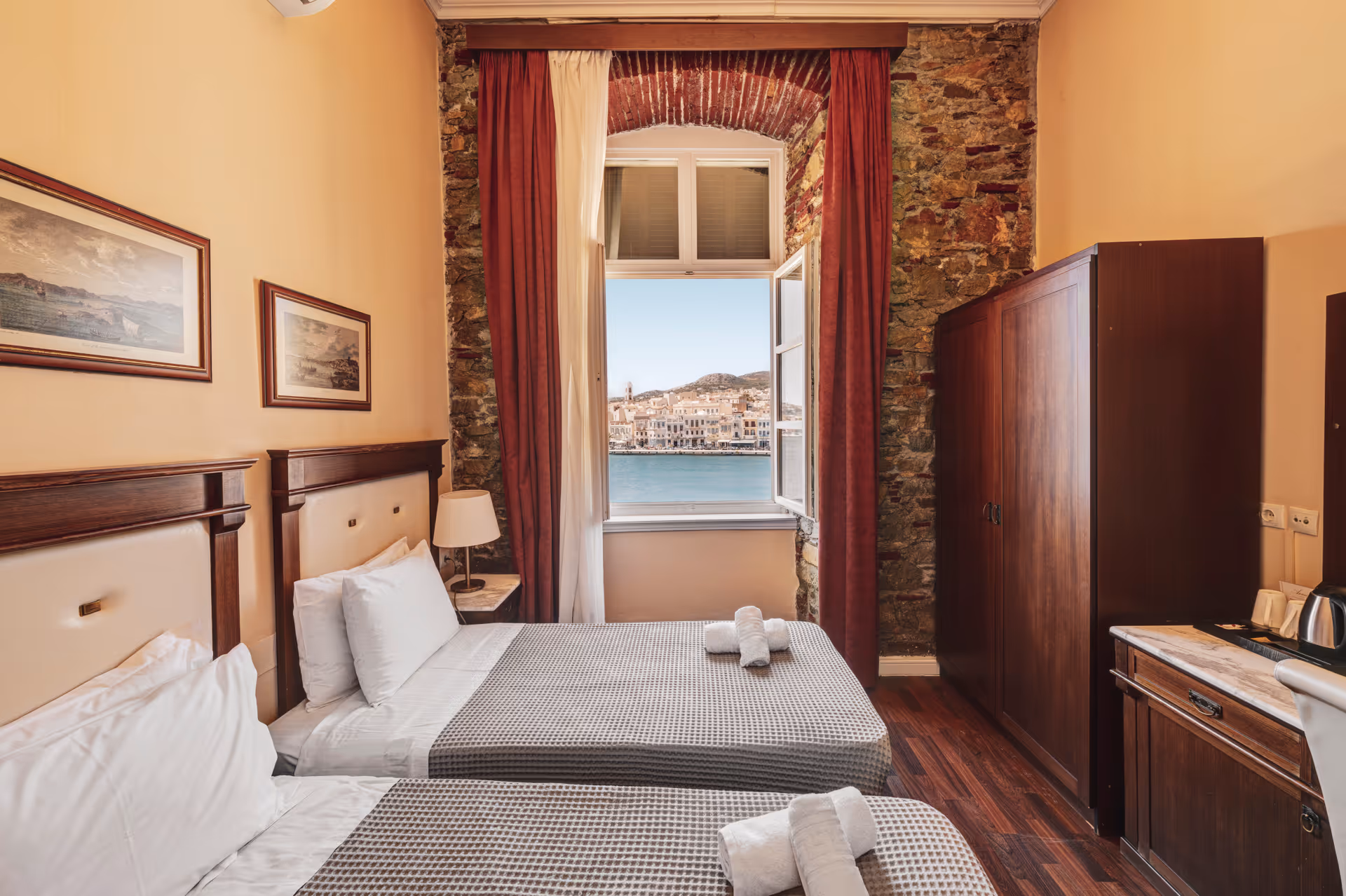 Hotel room with two single beds, a window with open curtains showing a waterfront town and hills.