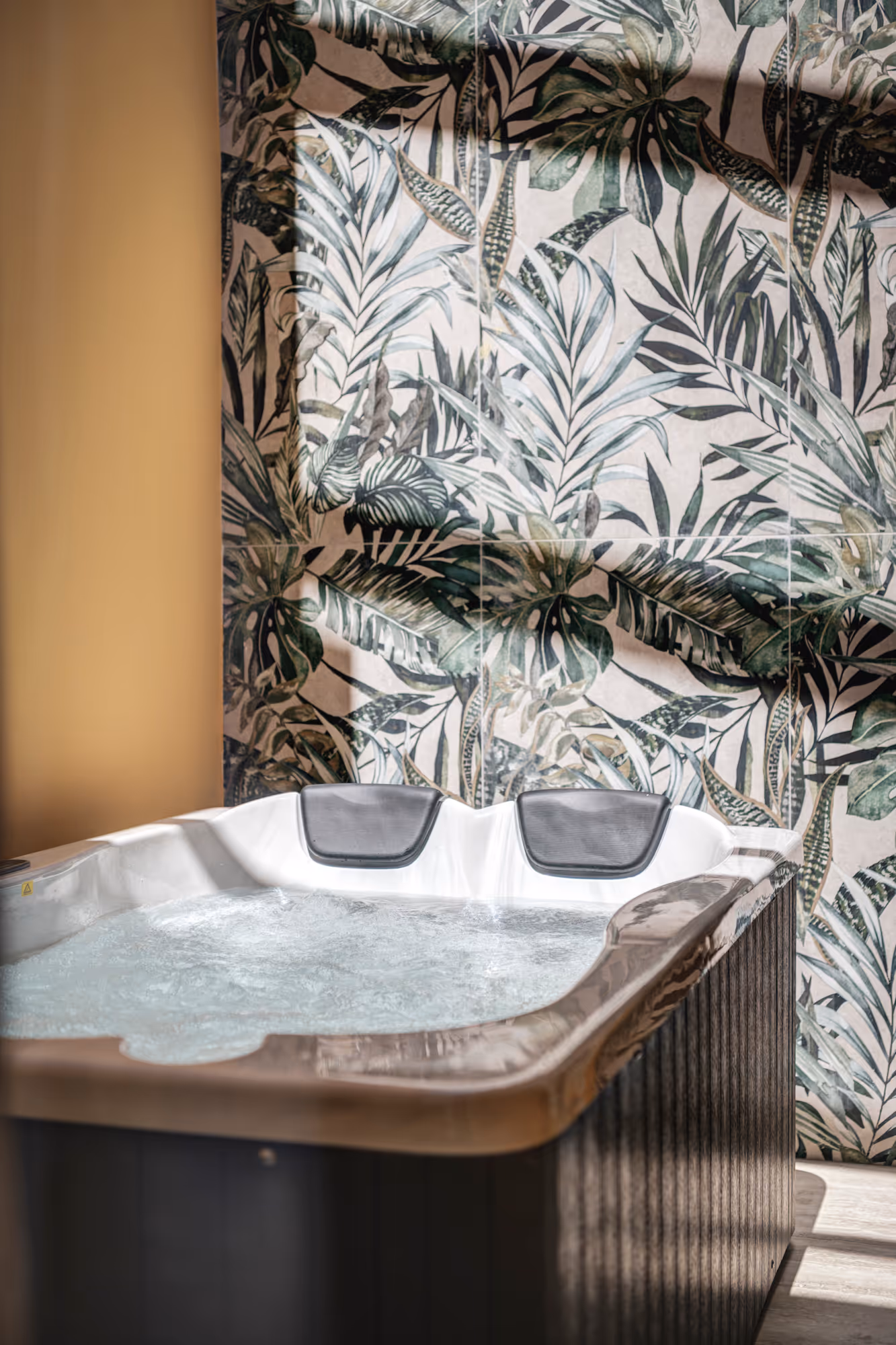 Indoor hot tub with bubbling water positioned against a wall with green tropical leaf patterned tiles.