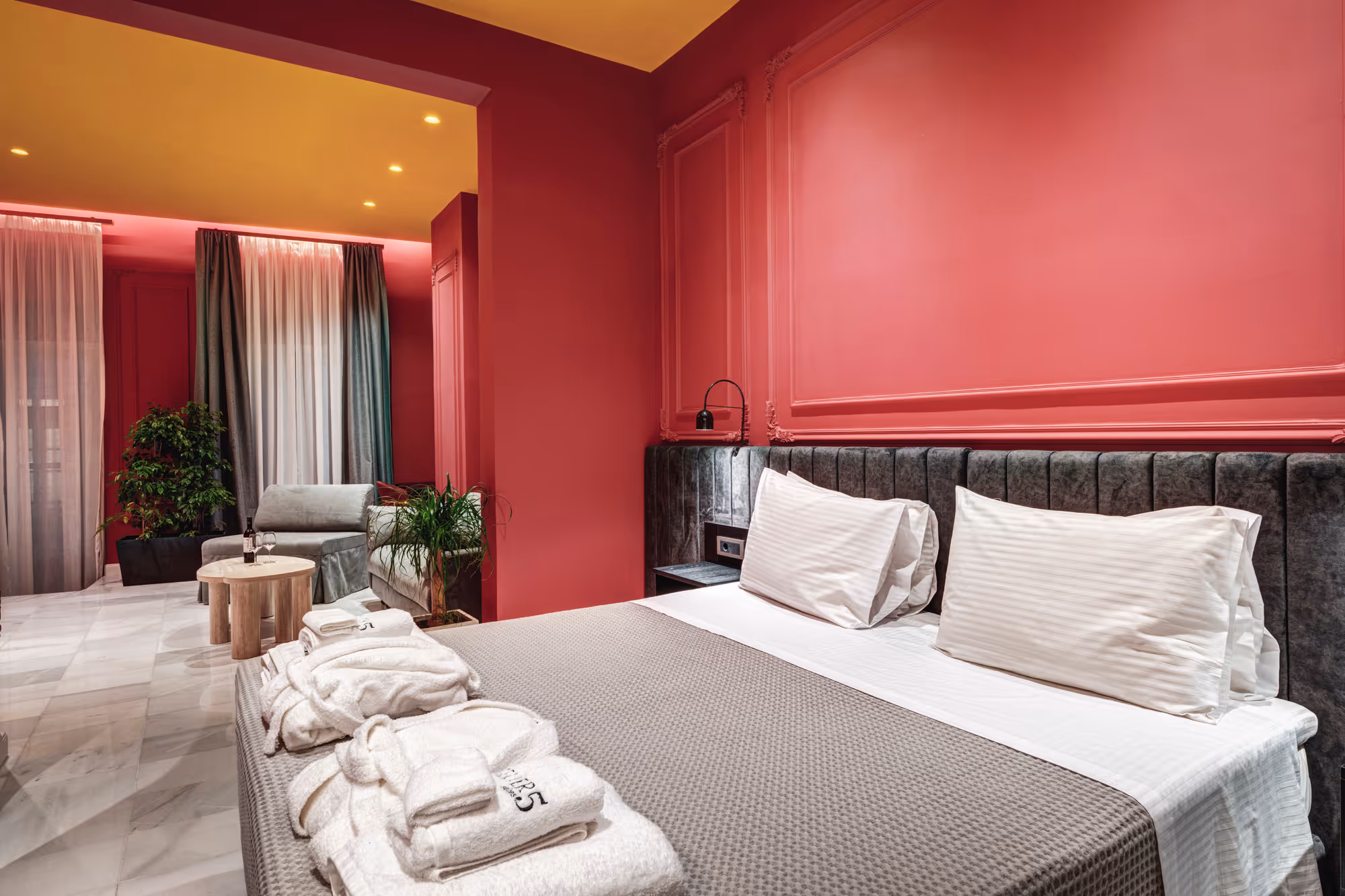 Modern bedroom corner with white striped pillows, textured bedding, black nightstand, and a wall-mounted lamp with power outlets.